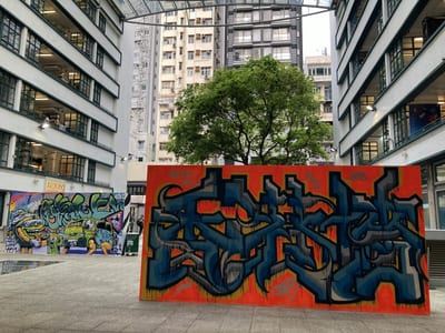A painted graffiti board standing in a courtyard, a tree behind it