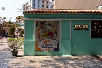 A mint green shop with old roof tiles and a painted poster in the window