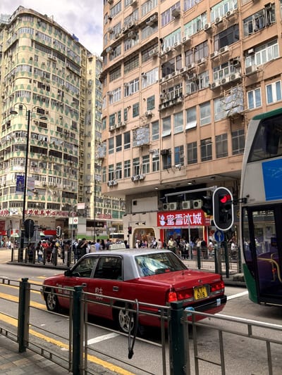 An old green-tiled tenement above a red taxi and a passing tram