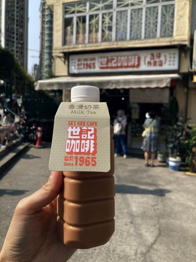 A bottle of milk tea held up in front of the cafe it came from