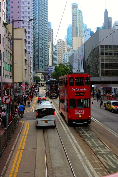 A red tram among cars and crowds on a Hong Kong street