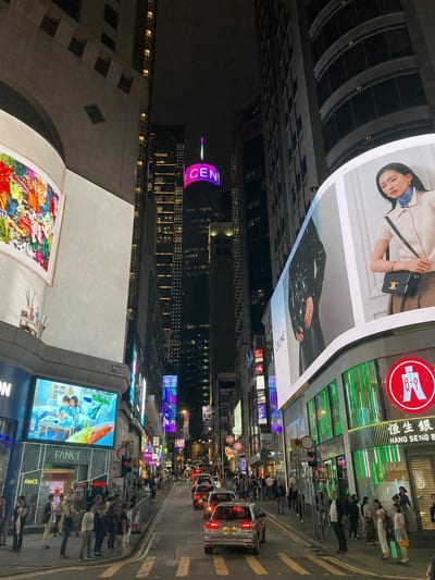 Central at night, neon and screens along the canyon of buildings