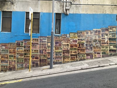 A mural of old Hong Kong tenements painted along a blue wall on a sloping street