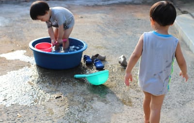 Two small children playing with a washtub of water in a concrete yard
